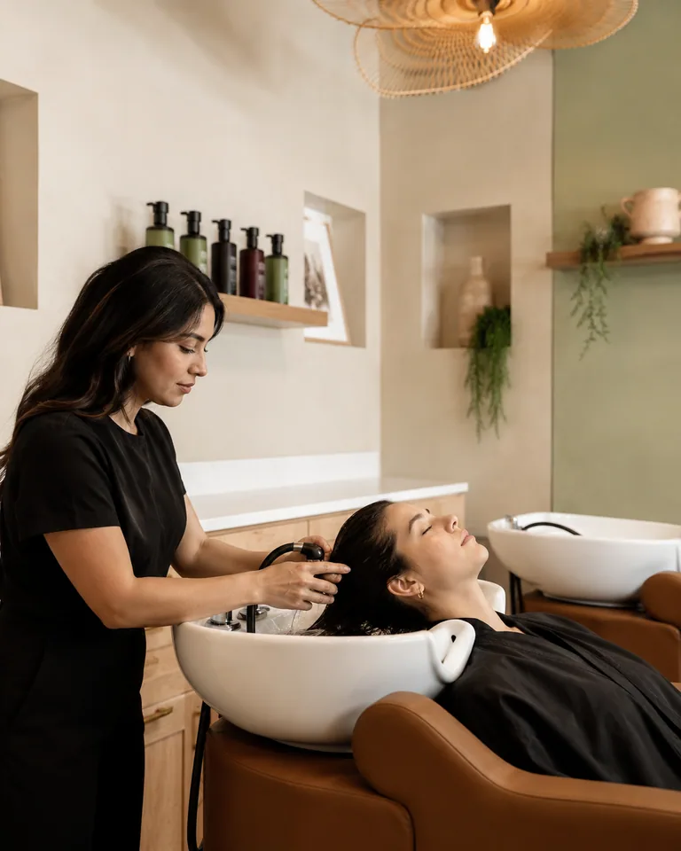A stylist rinsing a guest's hair at the shampoo station